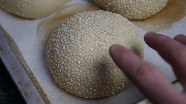 Męska dłoń sprawdza konsystencję bułki hamburgerowej